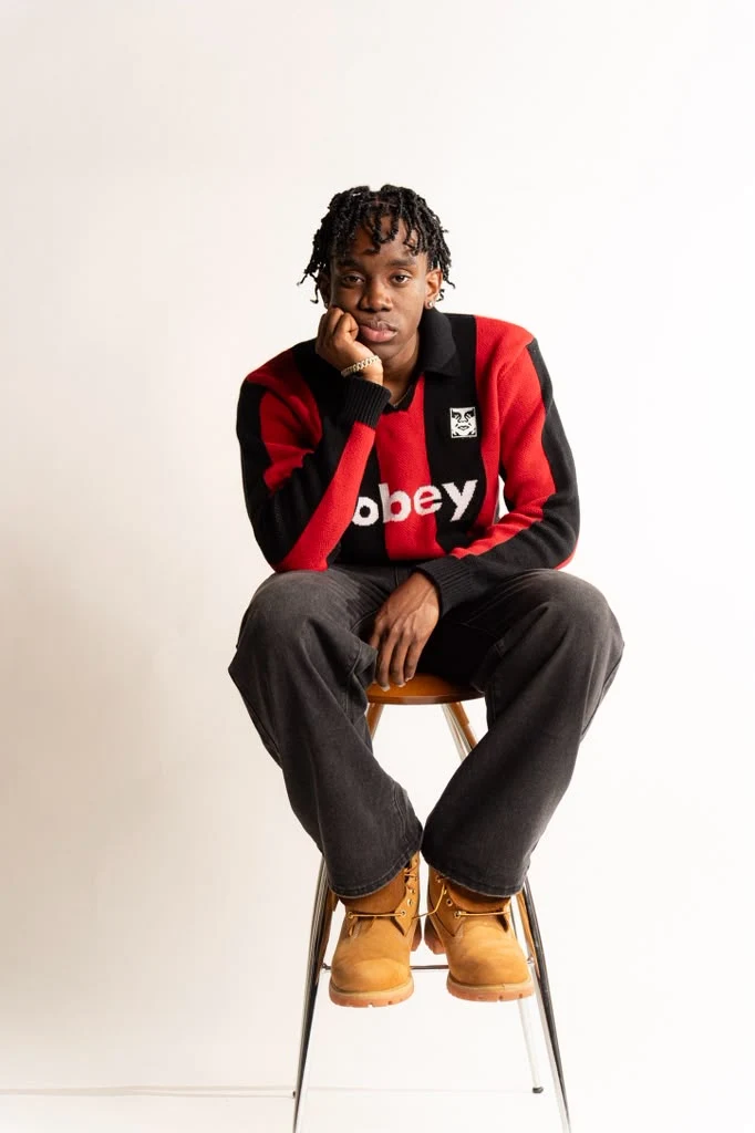 Ladi seated on a stool in a red and black sweater